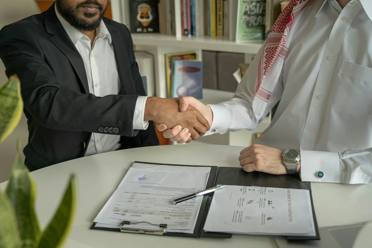 Two people shaking hands over a folder of signed forms